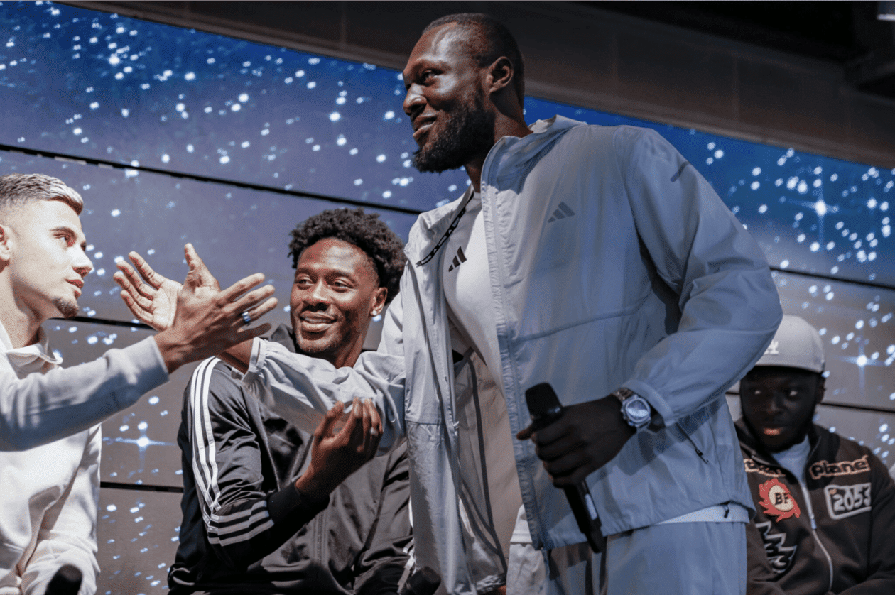 Stormzy holding a microphone and greeting two men on a stage.